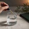 Un compte-gouttes de CBD à côté d’un verre d’eau